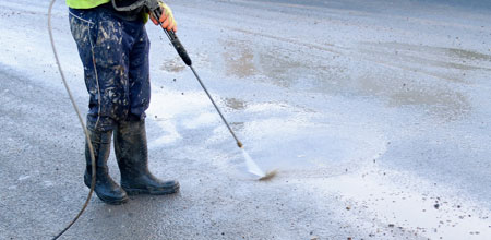 Man spraying pavement with strong sand and water blaster